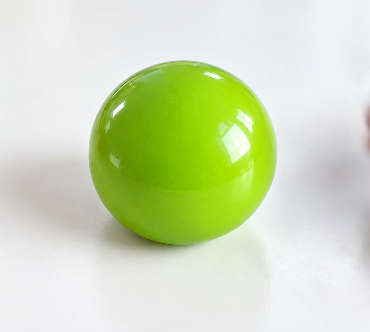 Ein glänzender grüner Wax-Cracking-Ball wird von zwei Händen zusammengedrückt, bis die Schale in Stücke bricht.